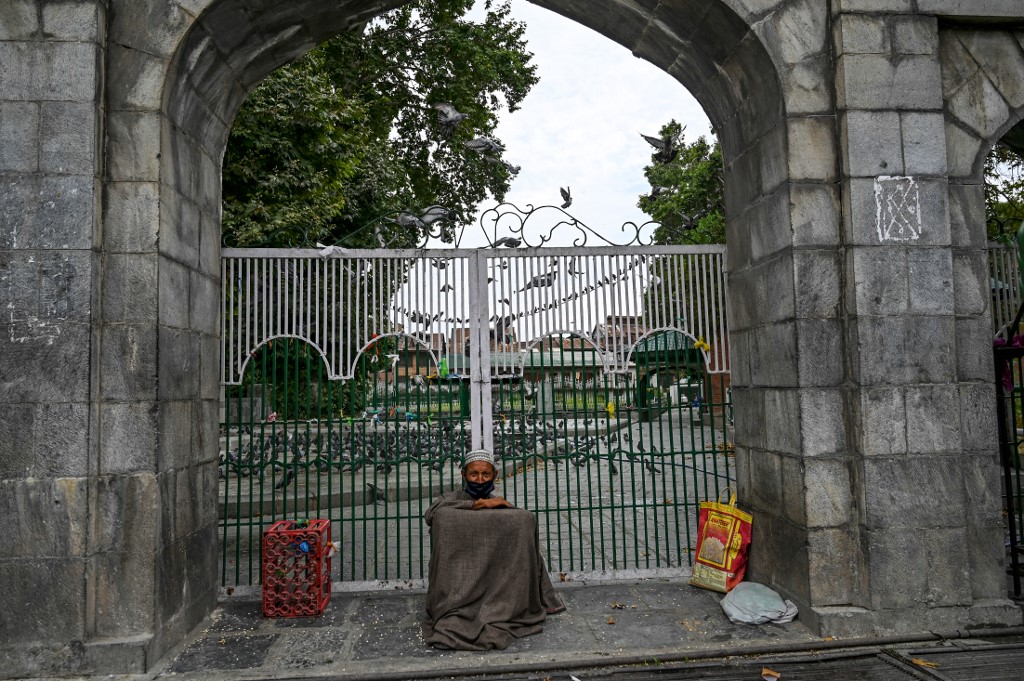 A man sits by a closed shrine amid Covid-19 restrictions in Srinagar on 1 August (AFP)