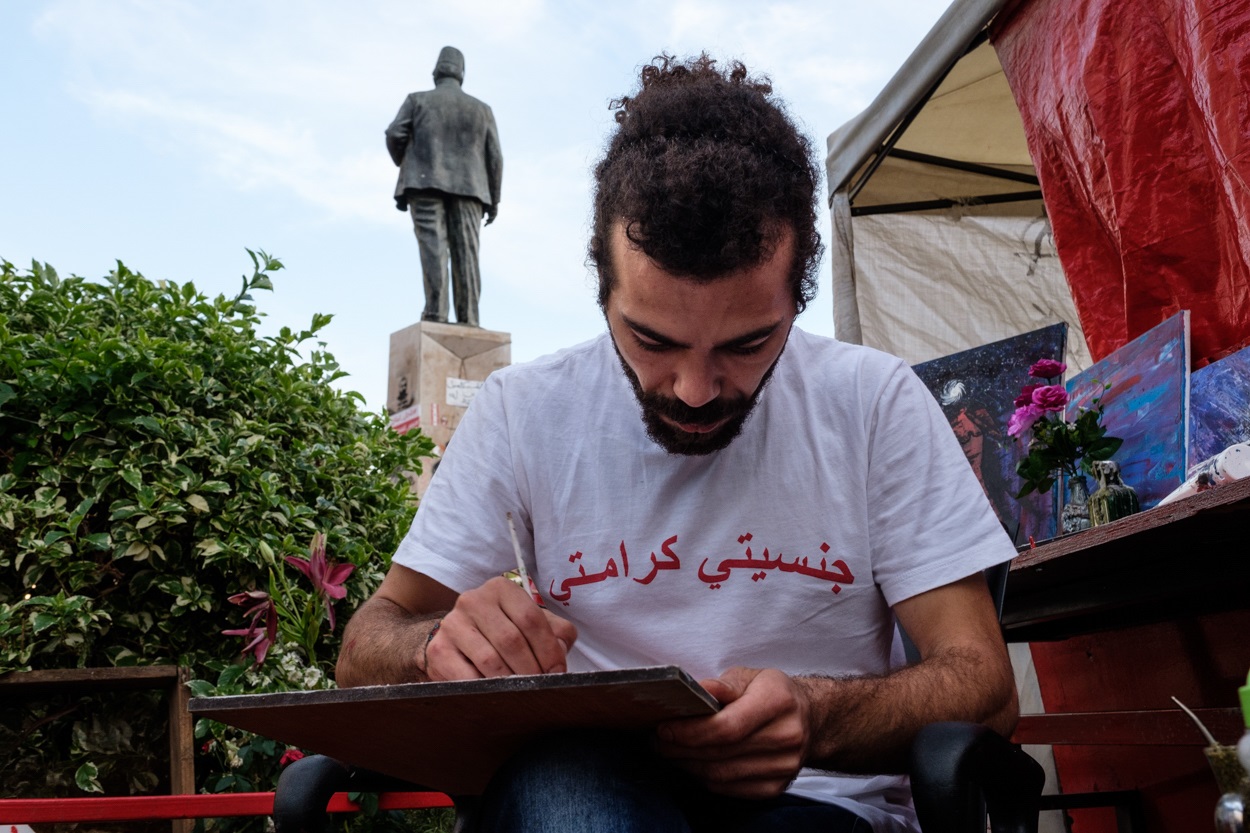 Mahmoud al-Khash, un manifestant né d’un père syrien et d’une mère libanaise, peint devant sa tente en portant un t-shirt « Jinsiyati, karamiti » – « Ma nationalité, ma dignité » (MEE/Rita Kabalan)