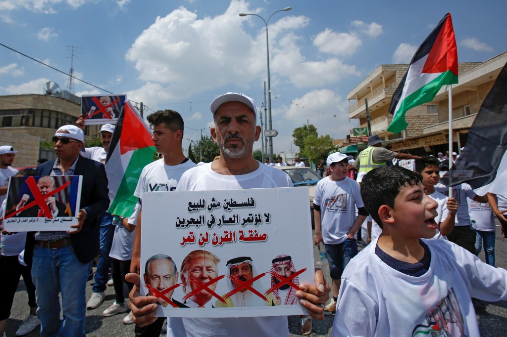 A Palestinian man holds up a sign criticising Israeli, US, Bahraini and Saudi leaders over the forthcoming Manama conference on 16 June in Bethlehem (AFP)