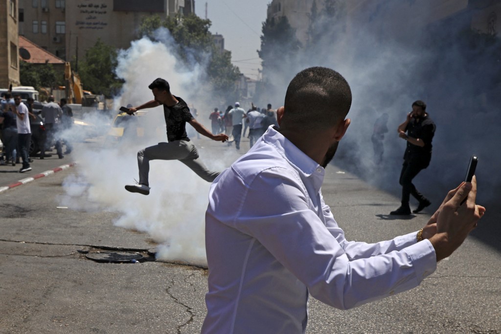 Protesters run from tear gas fired by Palestinian security forces during an anti-PA demonstration in Ramallah on 24 June 2021 (AFP)