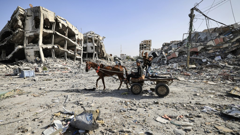 Palestinians ride on a cart as they inspect destroyed buildings on the southern outskirts of Gaza City on 26 November 2023 (AFP)