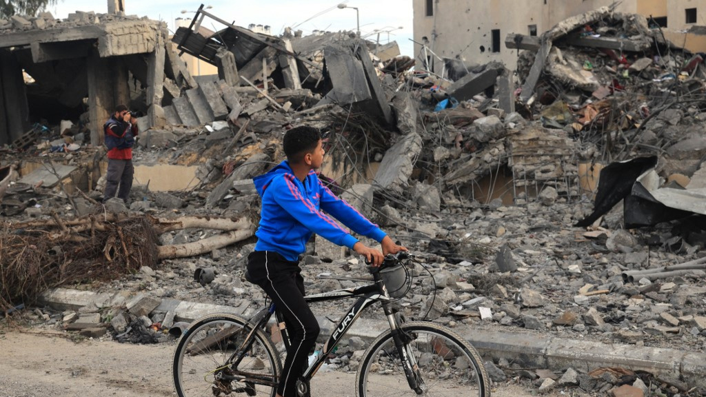 A Palestinian boy rides his bicycle past the rubble of a building after Israeli air strikes in Rafah, in the southern Gaza Strip, on 22 November 2023 (AFP)