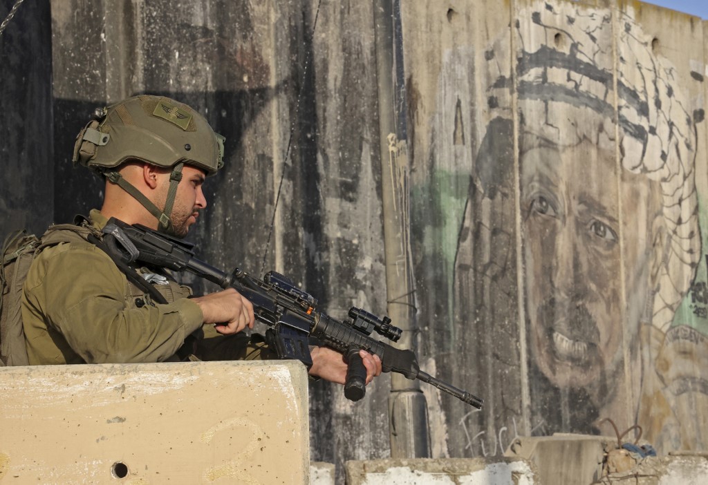 An Israeli soldier stands guard at the Qalandia checkpoint near a mural of late Palestinian leader Yasser Arafat on 30 April 2021 (AFP)