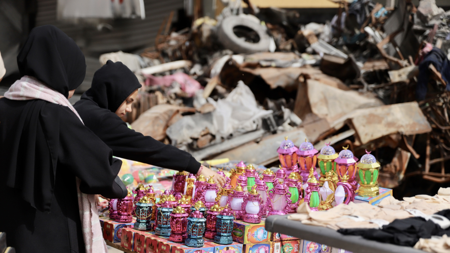 Palestinian girls pick lanterns from a stand in front of the destruction in Gaza City (Mohammed al-Hajjar/MEE)