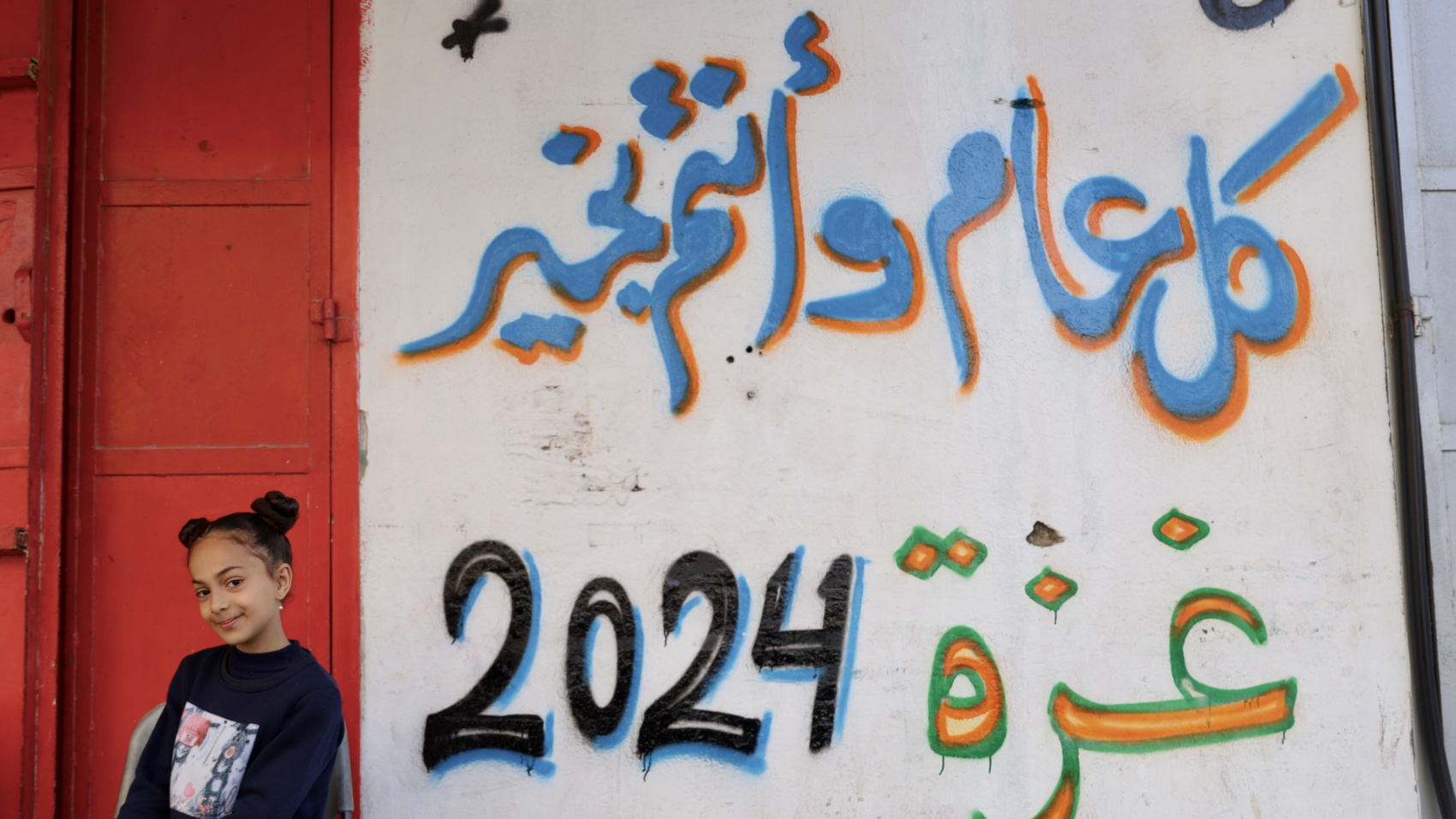 A girl stands in front of a wall painting that reads "many happy Ramadan returns" (Mohammed al-Hajjar/MEE).