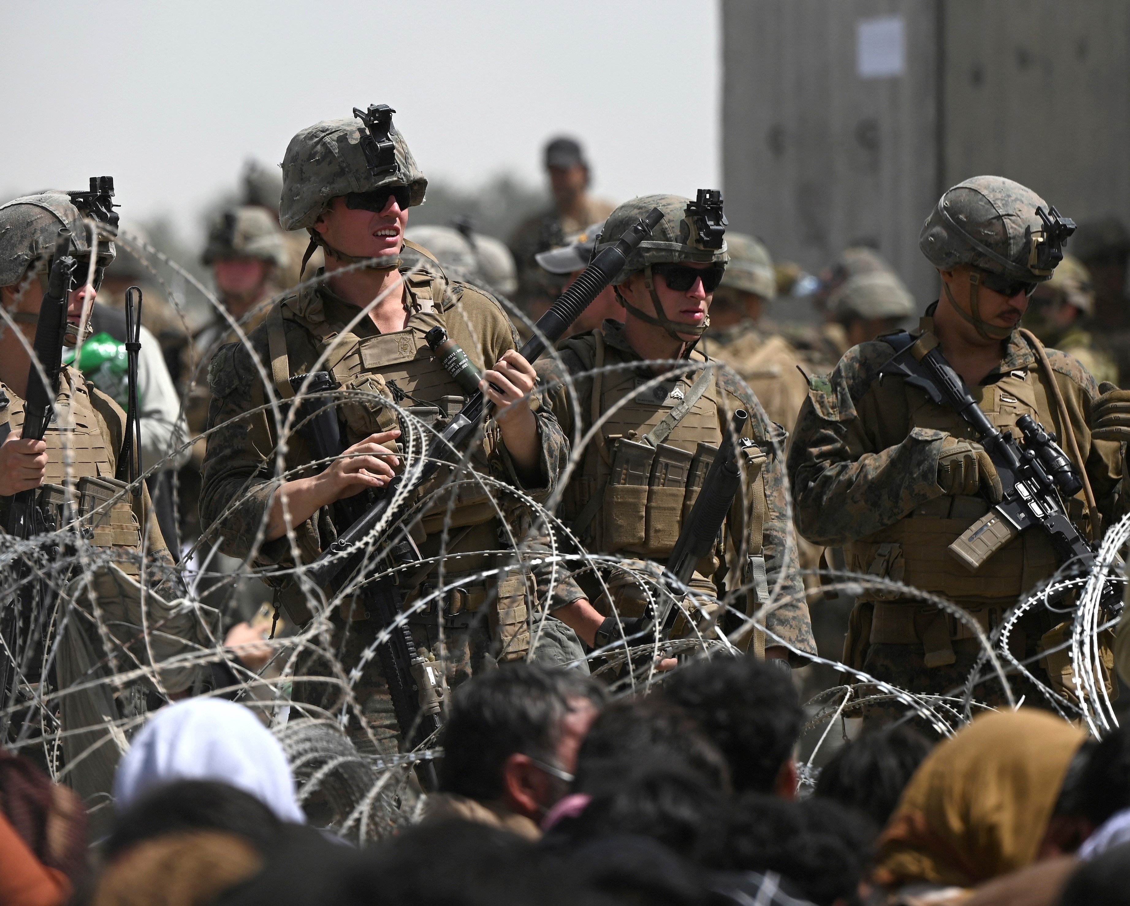 Des soldats américains montent la garde derrière des barbelés alors que des Afghans sont assis en bord de route près de la partie militaire de l’aéroport de Kaboul, le 20 août 2021 (AFP)