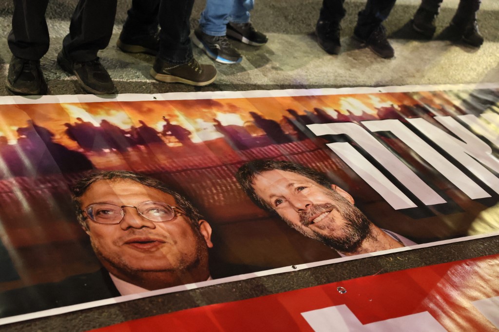 Israelíes junto a un cartel con los retratos de Itamar Ben-Gvir y Bezalel Smotrich durante una protesta contra el gobierno en Tel Aviv el 4 de marzo de 2023 (AFP)