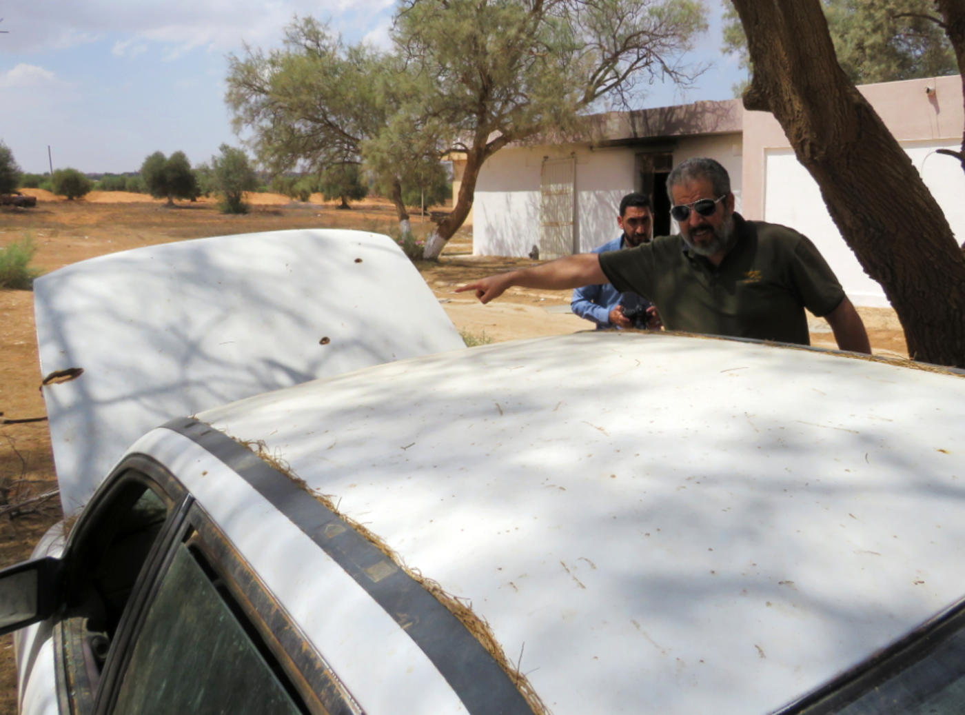 Mayor Mohammed Ali al-Kosher points at bulletholes in an abandoned car (MEE/Daniel Hilton)