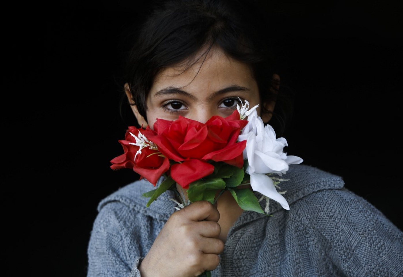 Une fillette palestinienne couvre sa bouche avec des fleurs en guise de masque, à Beit Lahia, au nord de Gaza, le 16 avril 2020 (AFP)