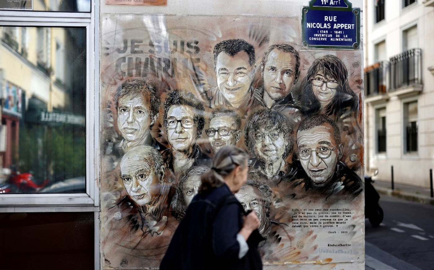 Une femme passe devant un tableau de l’artiste de rue et peintre français Christian Guemy, connu sous le nom de C215, en hommage aux membres du journal Charlie Hebdo tués par des islamistes extrémistes armés en janvier 2015, à Paris (AFP)