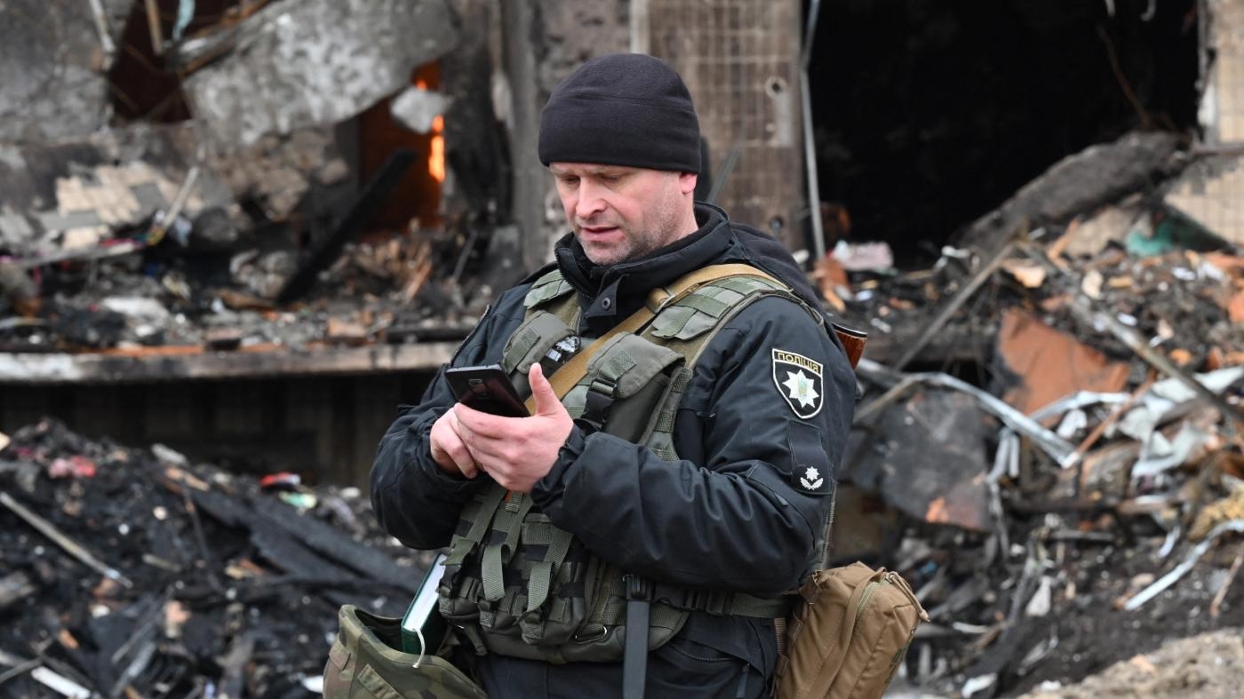 Un policier monte la garde devant un immeuble résidentiel détruit dans la capitale ukrainienne, Kiev, le 25 février 2022 (AFP)