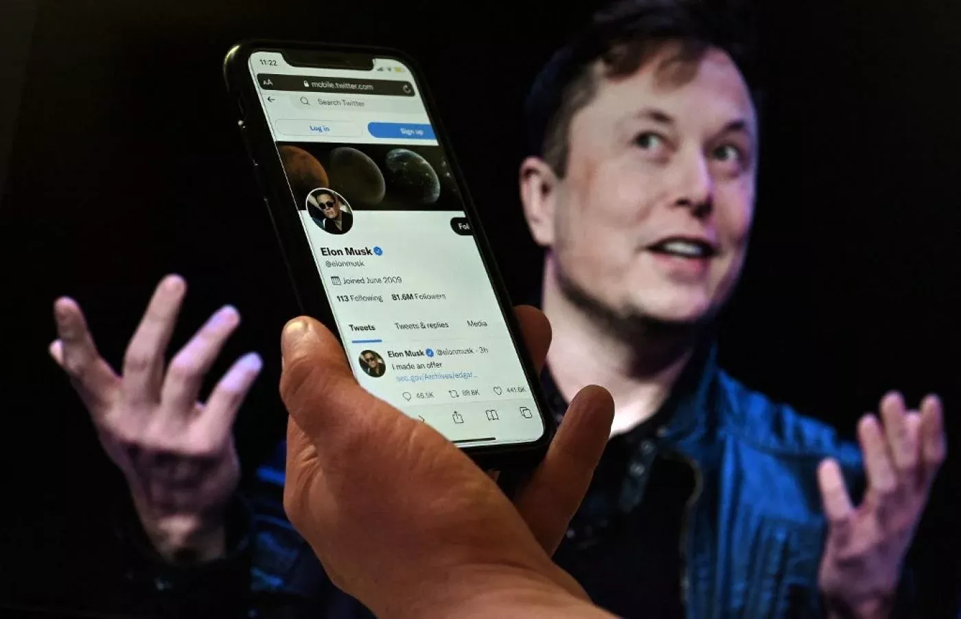 Un écran de téléphone affiche le compte Twitter d’Elon Musk tandis qu’une photo de lui est visible en arrière-plan, le 14 avril 2022 à Washington (AFP)