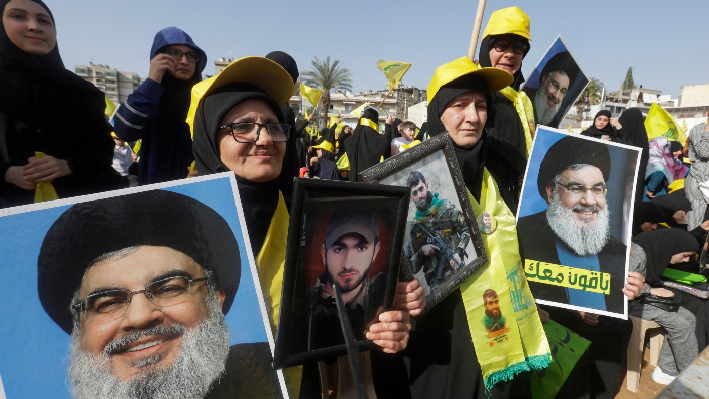 Supporters of Lebanon's Shi'ite group Hezbollah lift portraits of the group's leader Hassan Nasrallah as they rally to attend his speech, broadcast on a giant screen, in the southern city of Nabatiyeh, on 9 May, 2022 (AFP)