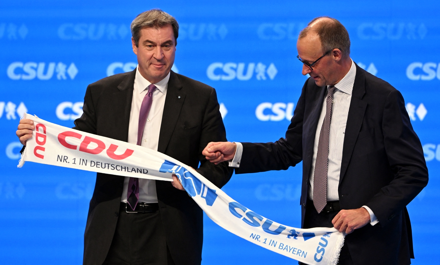 Bavaria's State Premier and leader of the conservative Christian Social Union (CSU) party Markus Soeder (L) and Germany's Christian Democratic Union (CDU) leader Friedrich Merz hold a scarf with their sister parties' logos at the CSU congress in Augsburg, Germany, on 29 October 2022 (AFP)