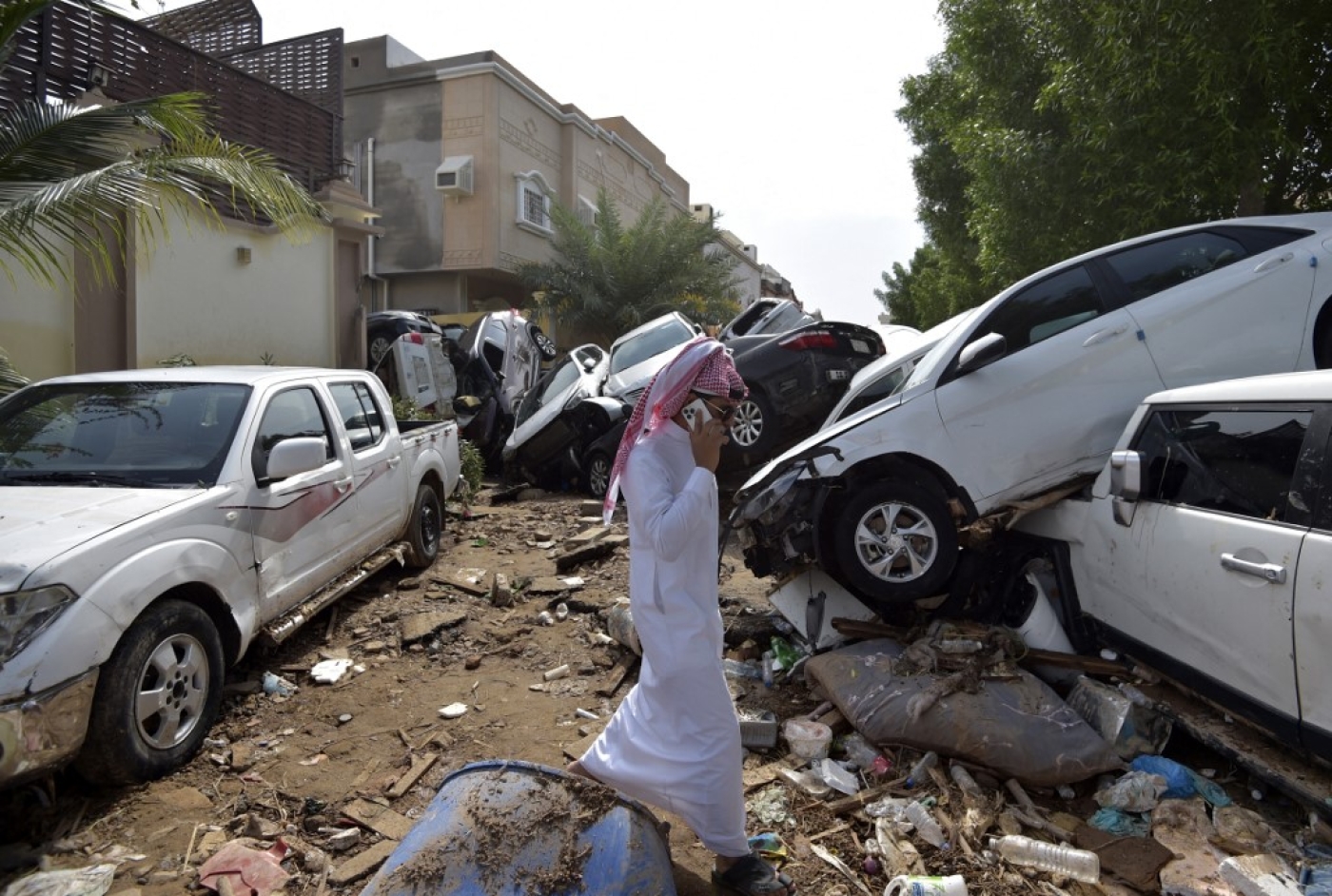 A man walks past cars piled up in a street after they were washed away by heavy rains in the Saudi coastal city of Jeddah on 25 November 2022 (AFP)