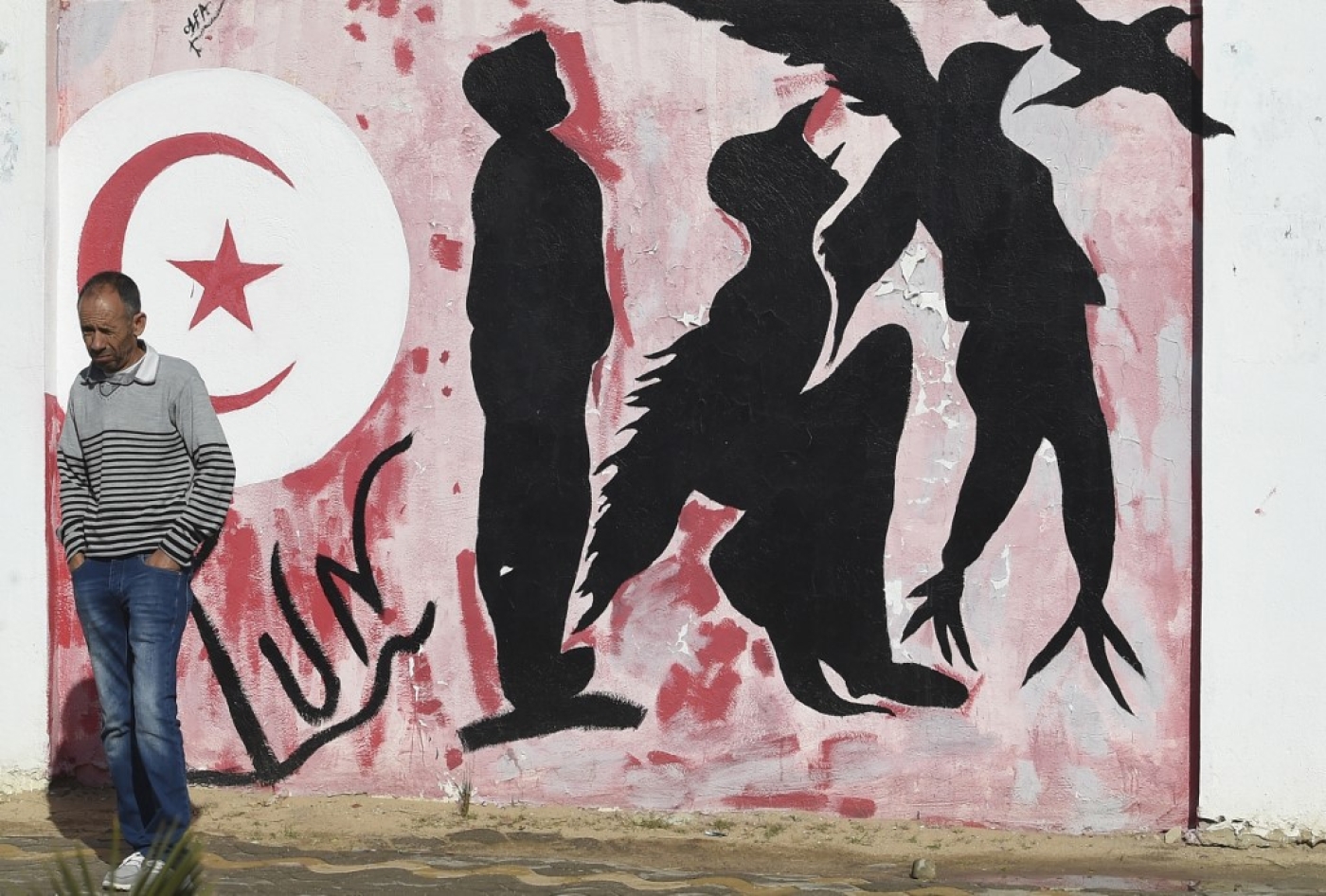 Un Tunisien attend près d’un graffiti représentant les silhouettes d’un homme se métamorphosant en oiseau symbolisant la liberté, place Mohamed Bouazizi, au centre de la ville de Sidi Bouzid le 27 octobre 2020, berceau de la révolution tunisienne de 2011 (AFP)