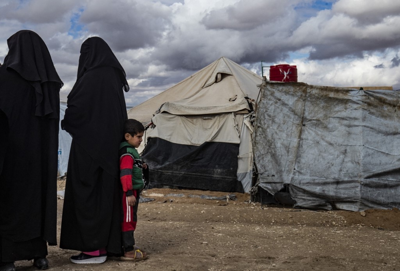 Des femmes et un enfant se tiennent près des tentes du camp kurde d’al-Hol qui abrite des proches présumés de combattants du groupe État islamique (Delil Souleiman/AFP)