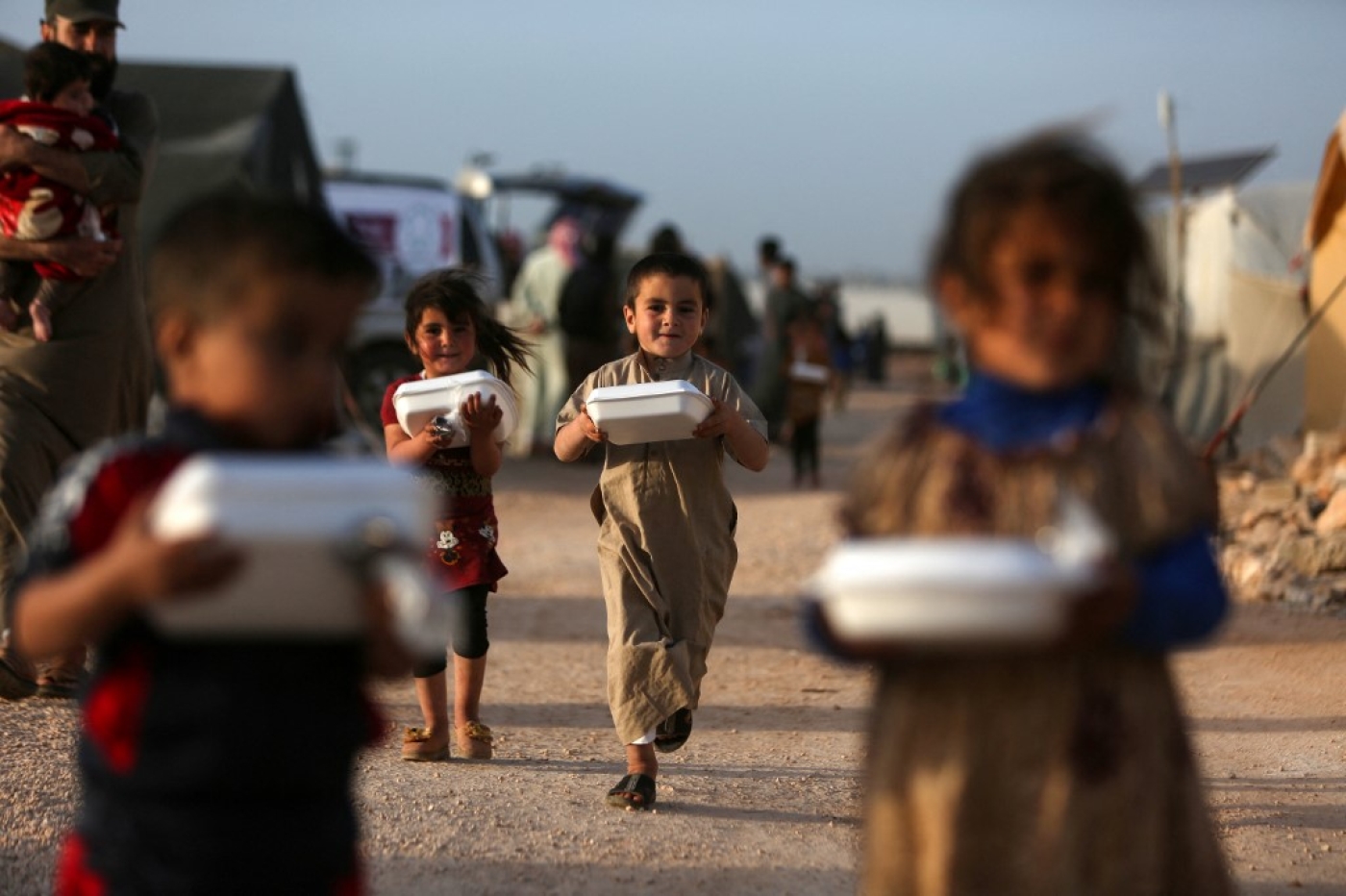 Des enfants syriens déplacés transportent des boîtes de nourriture distribuées par une organisation caritative locale avant l’iftar pendant le mois du Ramadan, dans un camp de déplacés de la province d’Idleb, le 3 avril 2022 (AFP)