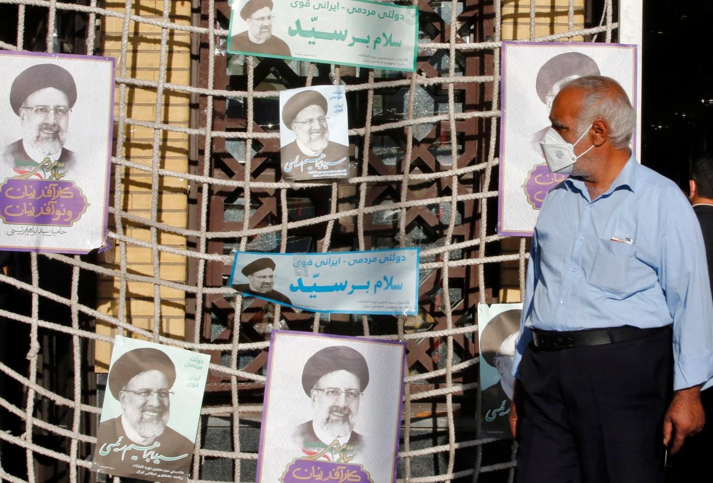 Un homme passe devant des affiches du candidat présidentiel Ebrahim Raïssi lors d’un meeting électoral à Téhéran, le 10 juin 2021 (AFP)