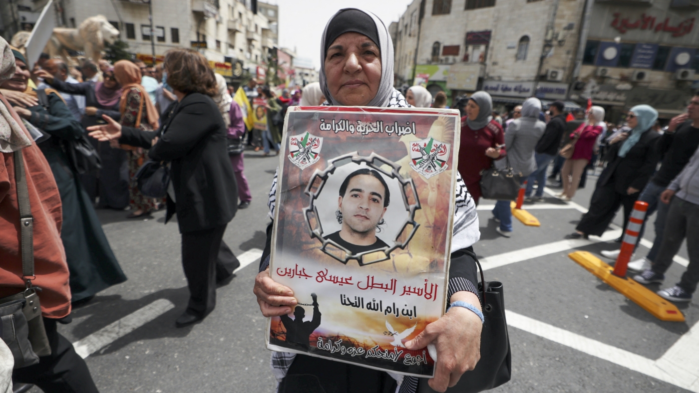 A woman carries a poster bearing the image of a jailed man during a demonstration marking Palestinian Prisoners' Day in Ramallah on 17 April 2022 (AFP)