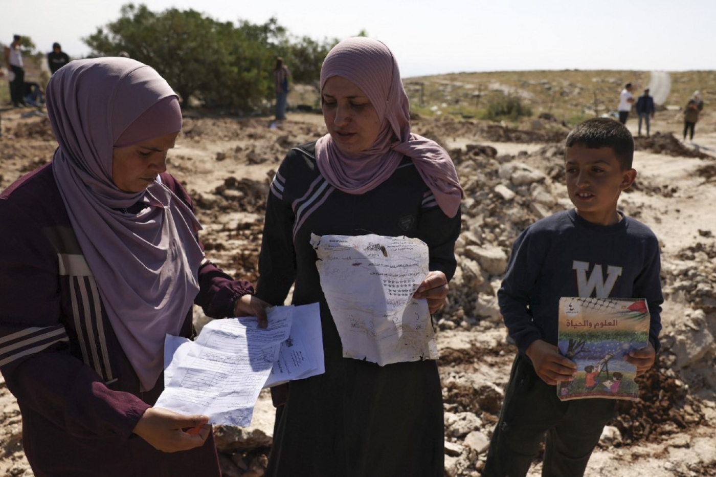 Palestinians pick up papers and books from the site of a school demolished by Israeli authorities in Jabbet al-Dhib, east of Bethlehem in the occupied West Bank, 7 May 2023 (AFP)