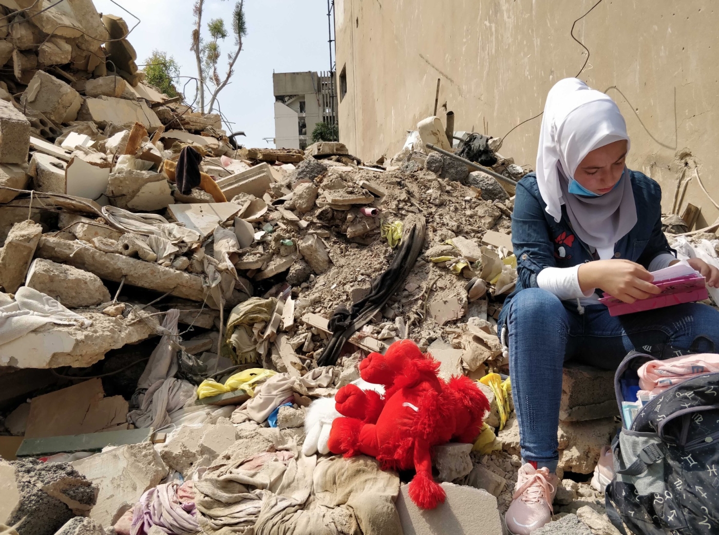 Dima, a Syrian refugee, visits her collapsed home, recovering her backpack and a teddy she found in the rubble after the explosion (MEE/Nadda Osman)