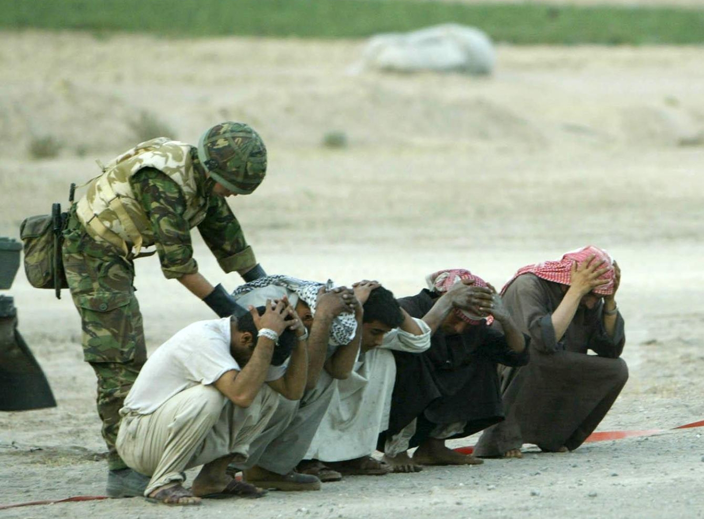 A British soldier searches Iraqis at a checkpoint on the road to Basra in 2003