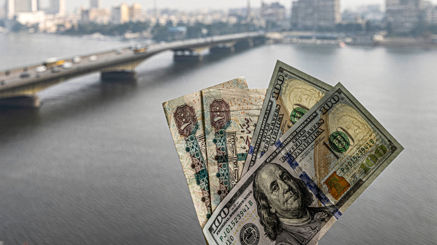 Two pairs of US hundred dollar and Egyptian hundred pound notes are held before a window showing the skyline of Egypt's capital Cairo and the Nile river on 16 January 2023 (AFP)