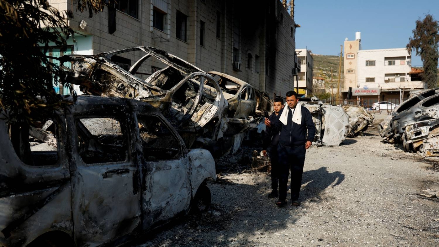 Palestinians walk near cars burned in an attack by Israeli settlers in the occupied West Bank on 27 February 2023.