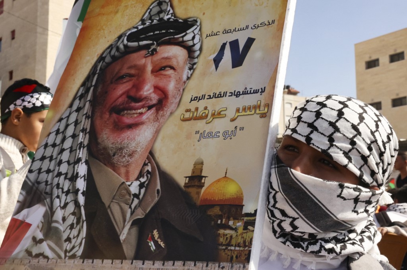Palestinian supporters of the Fath movement raise a poster of the late leader Yasser Arafat during a rally marking the 17th anniversary of his passing, in the village of Halhul, north the West Bank town of Hebron, on 11 November 2021 (AFP)