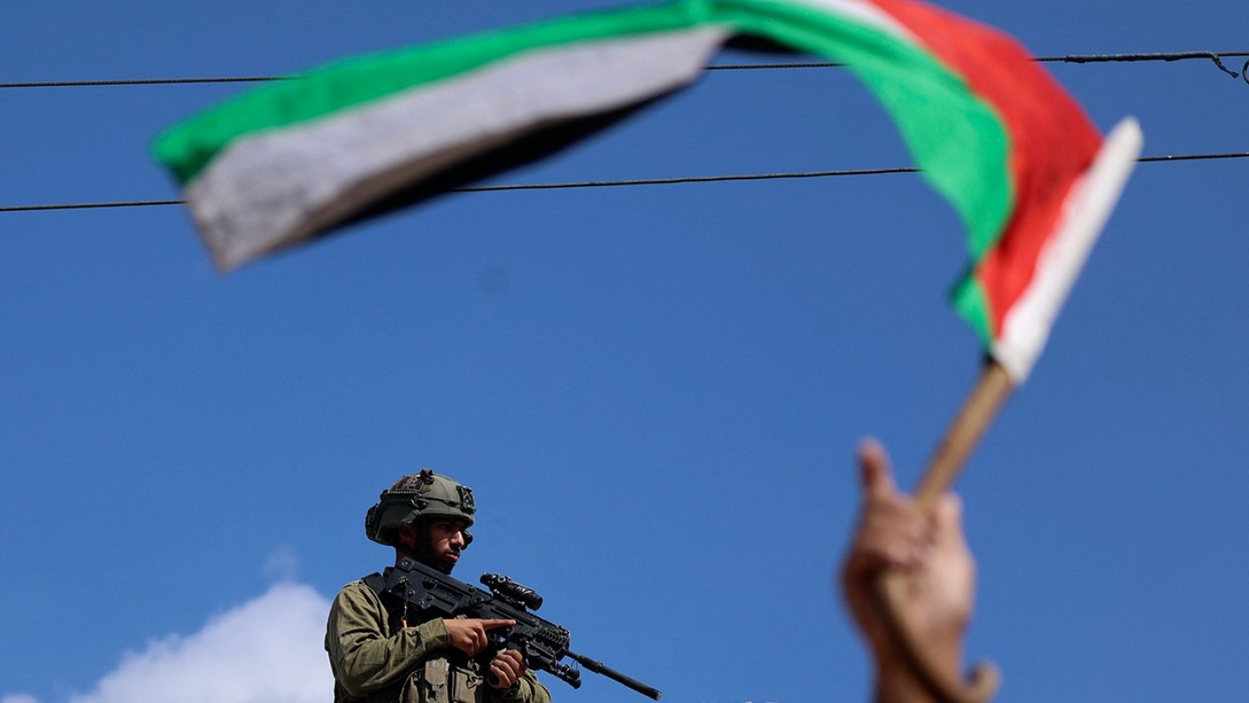 A man waves a Palestinian flag while an Israeli solder looks on during clashes in the village of Deir Sharaf near the western entrance of the city of Nablus in the occupied West Bank on 20 October, 2022 (AFP)