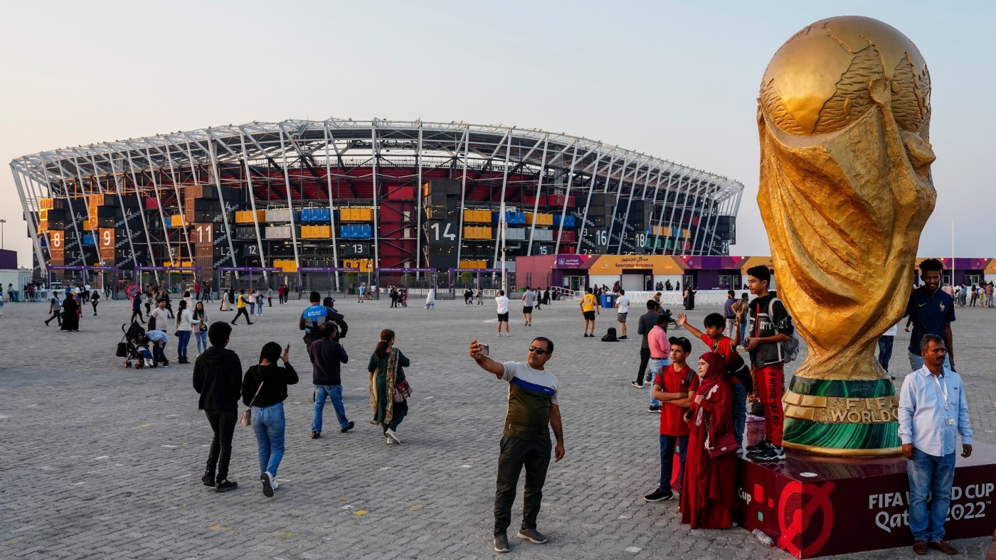 People pose for pictures next to a replica of the World Cup Trophy with the Stadium 974 in the background on 16 December 2022 (Associated Press)