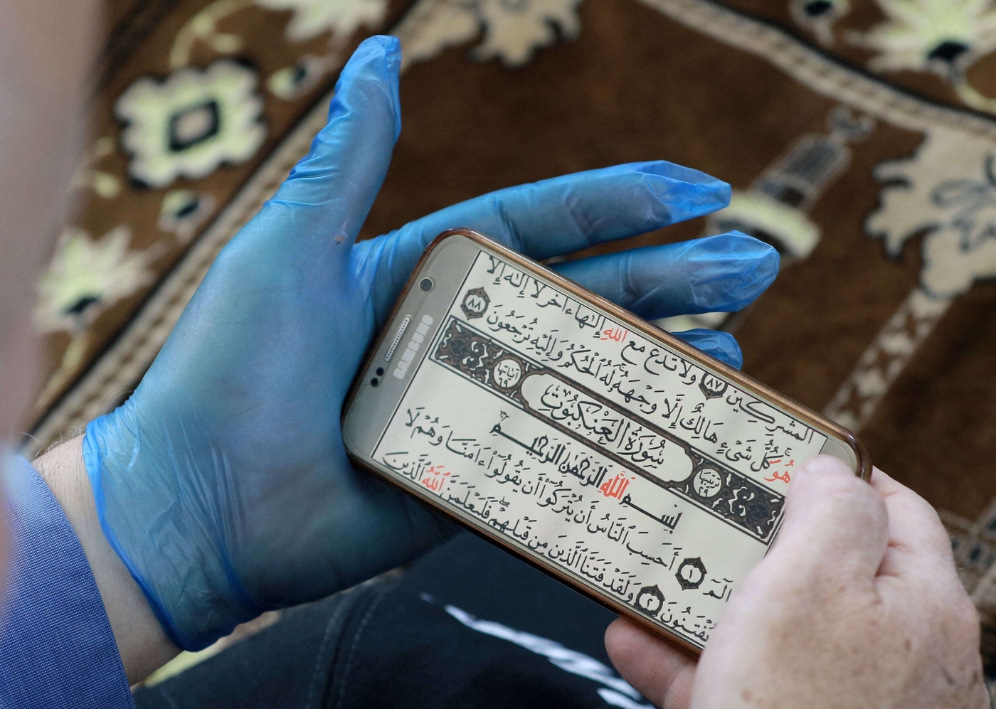 A man wearing gloves reads the Holy Qur'an from an app inside the Mohammad al-Tilawy Mosque in Amman, Jordan. (AFP)