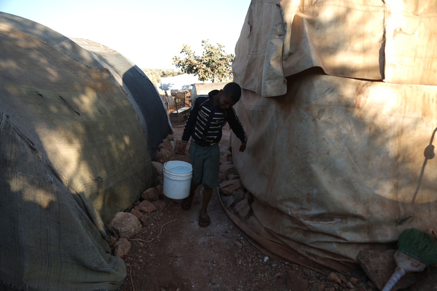 A child transfers water with a bucket from the open water tank to his tent in the IDP camp in Killi town, Idlib countryside, 14 September 2022 (MEE/Ali Haj Suleiman)