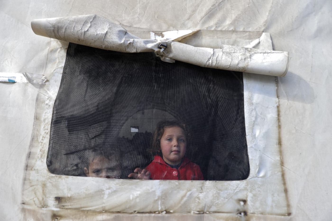 Des petits Syriens regardent par la fenêtre d’une fenêtre de tente, dans un abri d’urgence, au nord de la province d’Idleb, tenue par les rebelles, un jour après les séismes qui ont frappé la Turquie et la Syrie (AFP/Abdulaziz Ketaz)