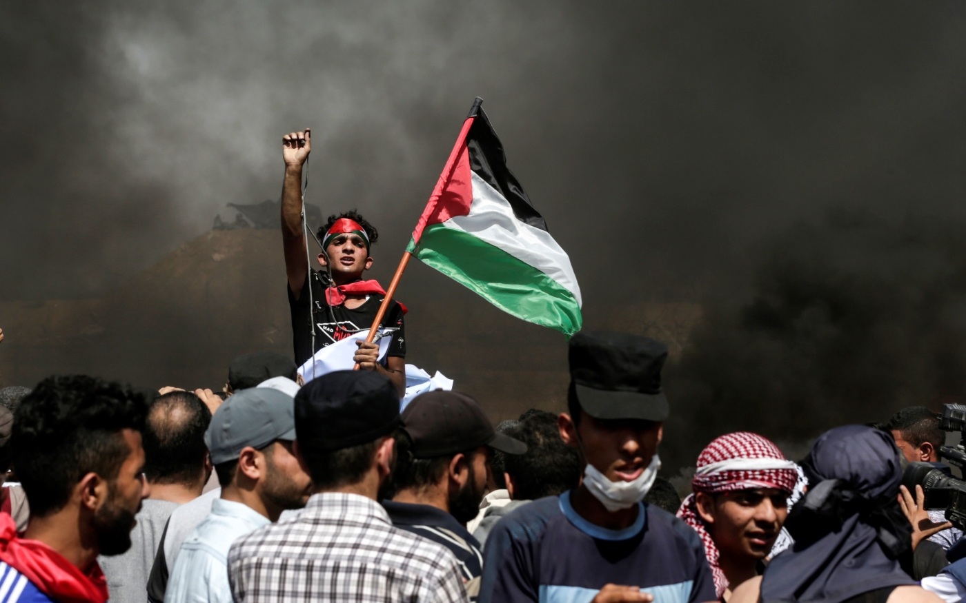 Un manifestant palestinien agite son drapeau national alors que la fumée s’élève de pneus en feu lors d’une manifestation le long de la frontière entre la bande de Gaza et Israël, le 8 juin 2018 (AFP)