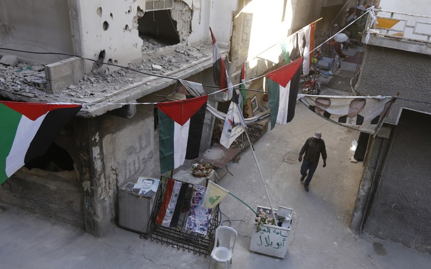 Un homme passe à côté de bâtiments détruits ornés de drapeaux palestiniens dans le camp de réfugiés palestiniens de Yarmouk, au sud de Damas (AFP)