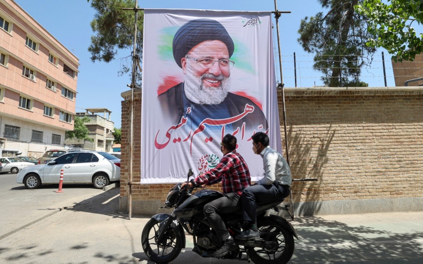 Des Iraniens passent devant un poster d’Ebrahim Raïssi, à Téhéran, le 29 mai 2021 (AFP/Atta Kenare)