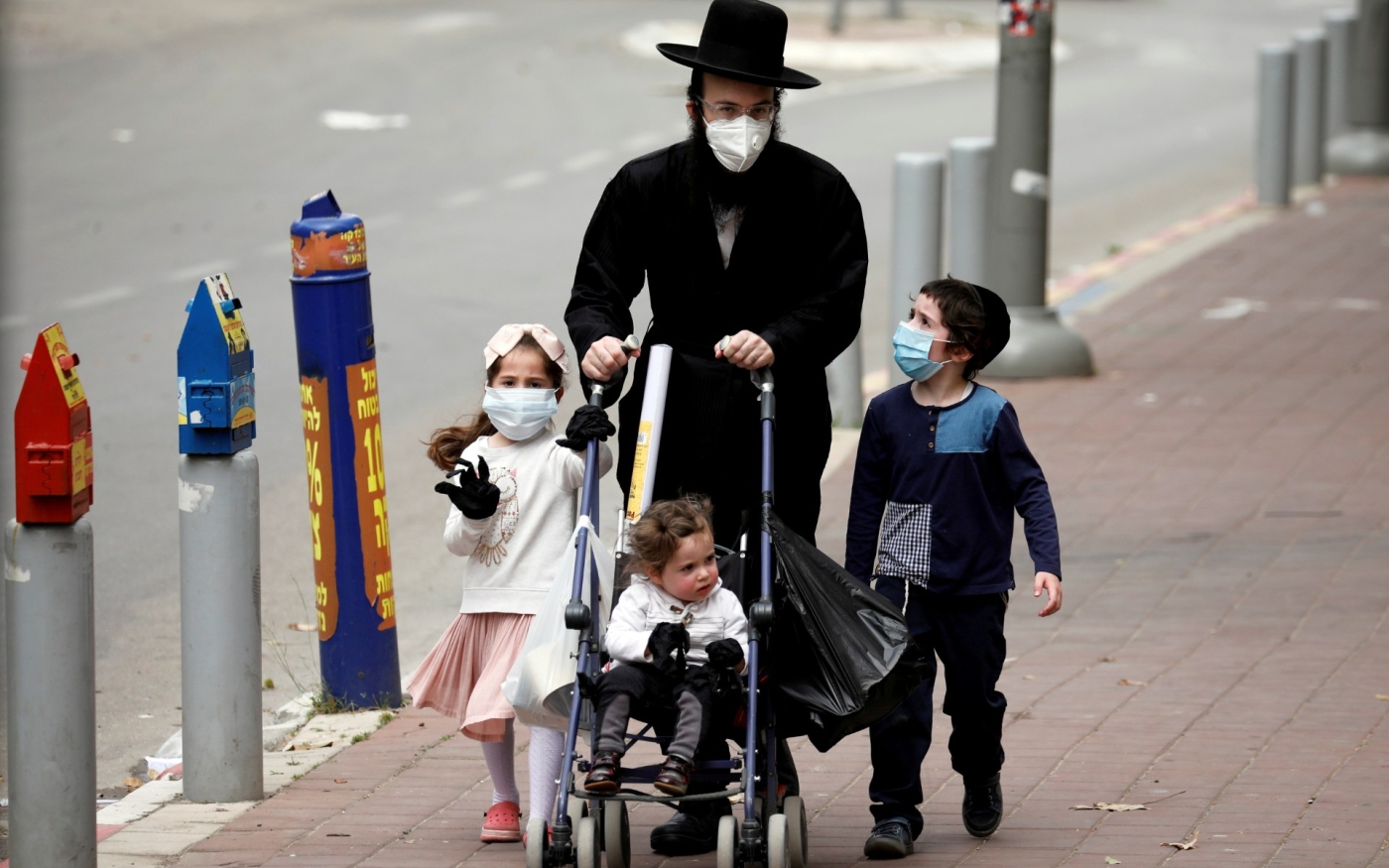 Des membres d’une famille juive ultra-orthodoxe équipés de masques marchent sur un trottoir à Bnei Brak (Reuters)