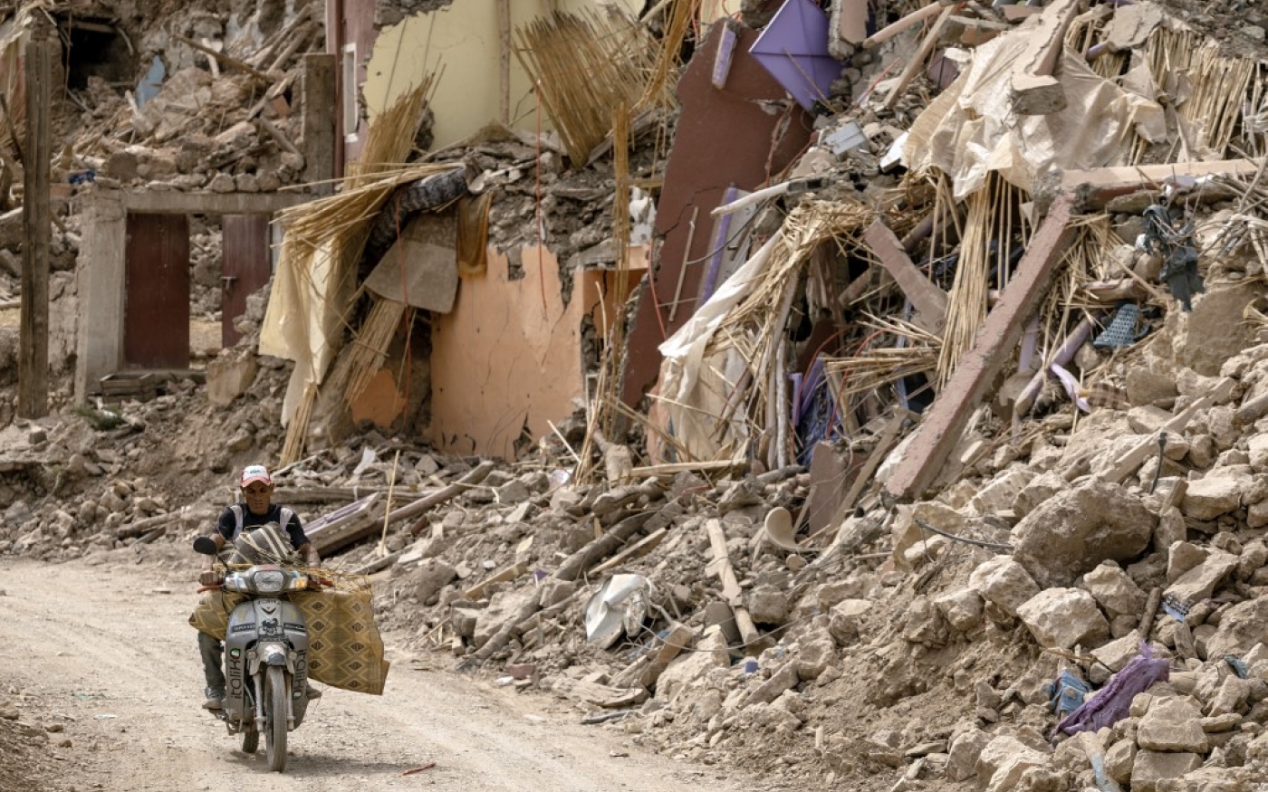 Un homme conduit sa moto à côté des décombres dans le village d’Imi N’Tala, dans le centre du Maroc, frappé par le tremblement de terre, le 5 octobre 2023 (AFP/Fadel Senna)