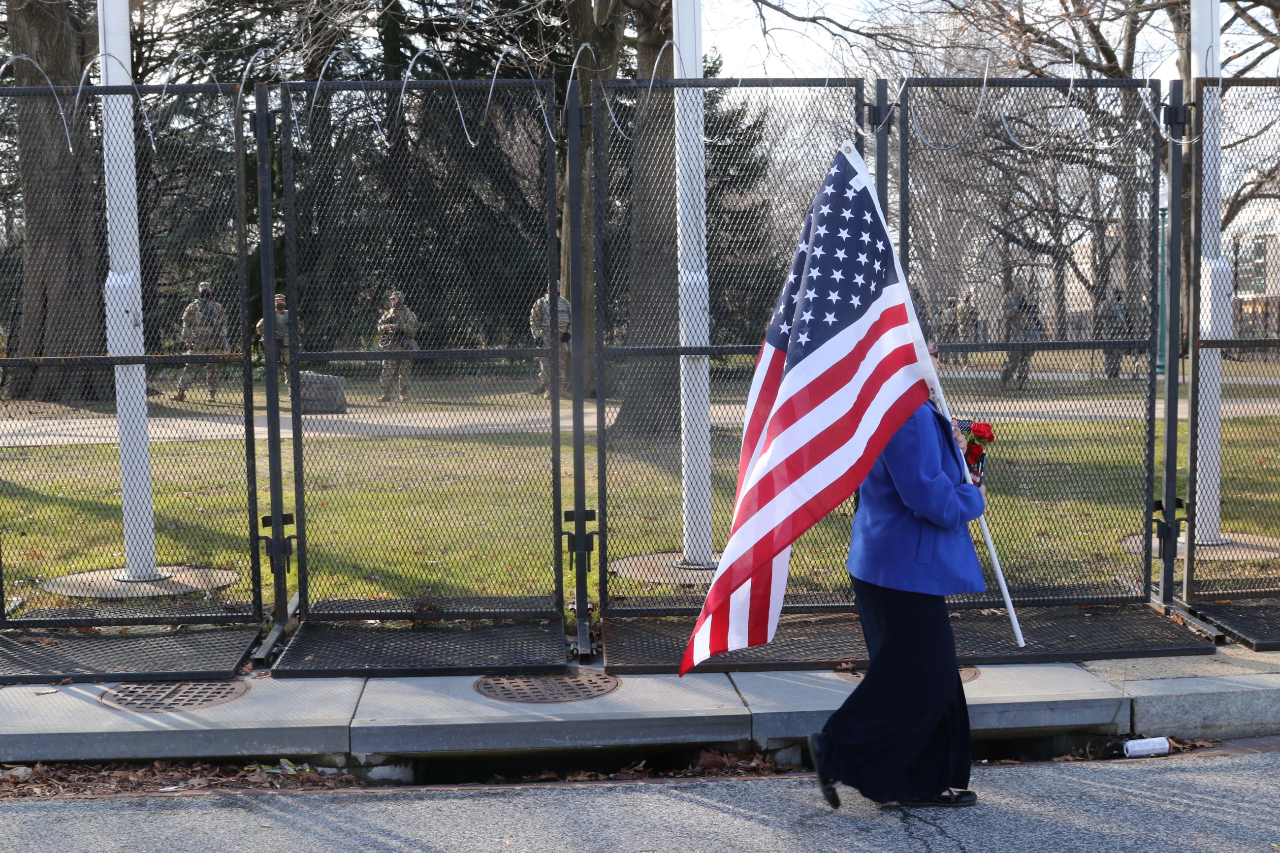 A woman walks past a line of soldiers while carrying the American flag.