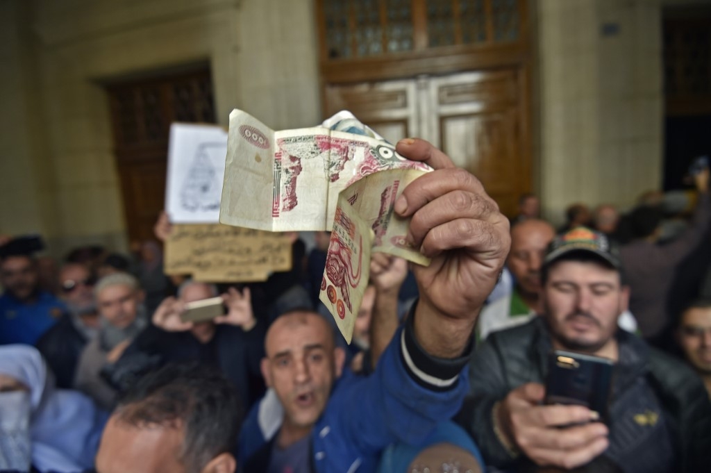Un Algérien agite des billets de banque alors qu’une foule attend à l’entrée du tribunal, à Alger le 2 décembre 2019, avant l’ouverture d’un procès pour corruption d’anciennes personnalités politiques et économiques (AFP)