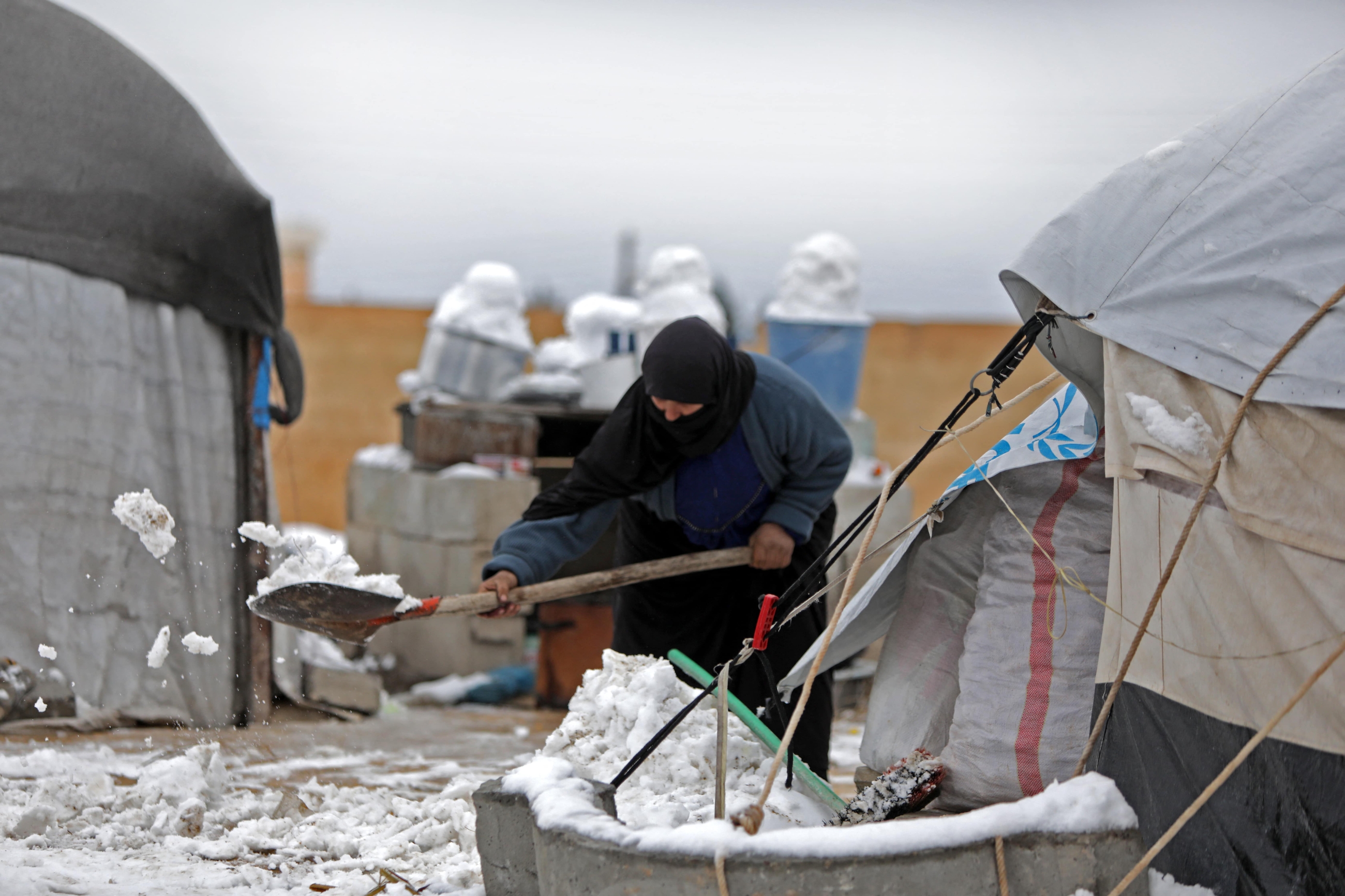 A woman who fled pro-regime forces attacks in northeastern Syria, clears the snow in front of a tent at camp for displaced people in the northern Syrian town of Tal Abyad by the border with Turkey, on February 13, 2020. (Bakr ALKASEM/AFP)