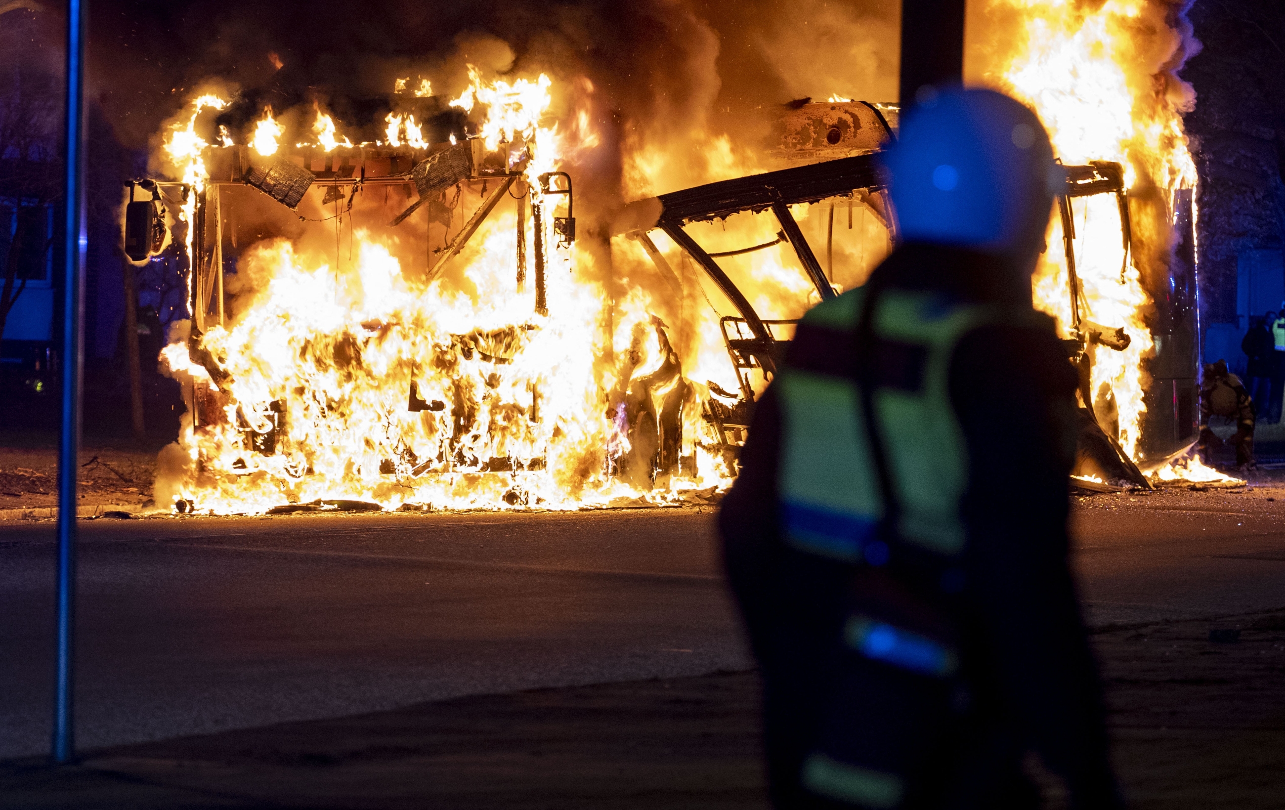 An anti-riot police officer watches a city bus burning in Malmo on 16 April 2022 (AFP)