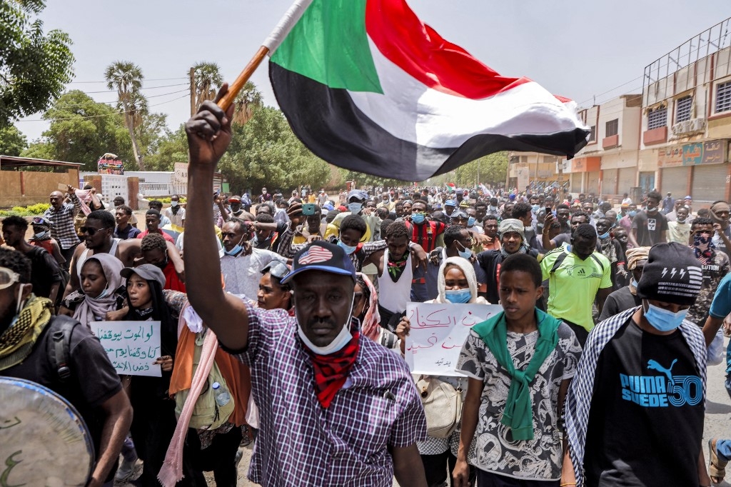 An anti-coup protester waves a Sudanese national flag while marching with others during mass demonstrations against military rule in the centre of Sudan's capital Khartoum on June 30, 2022 (AFP)