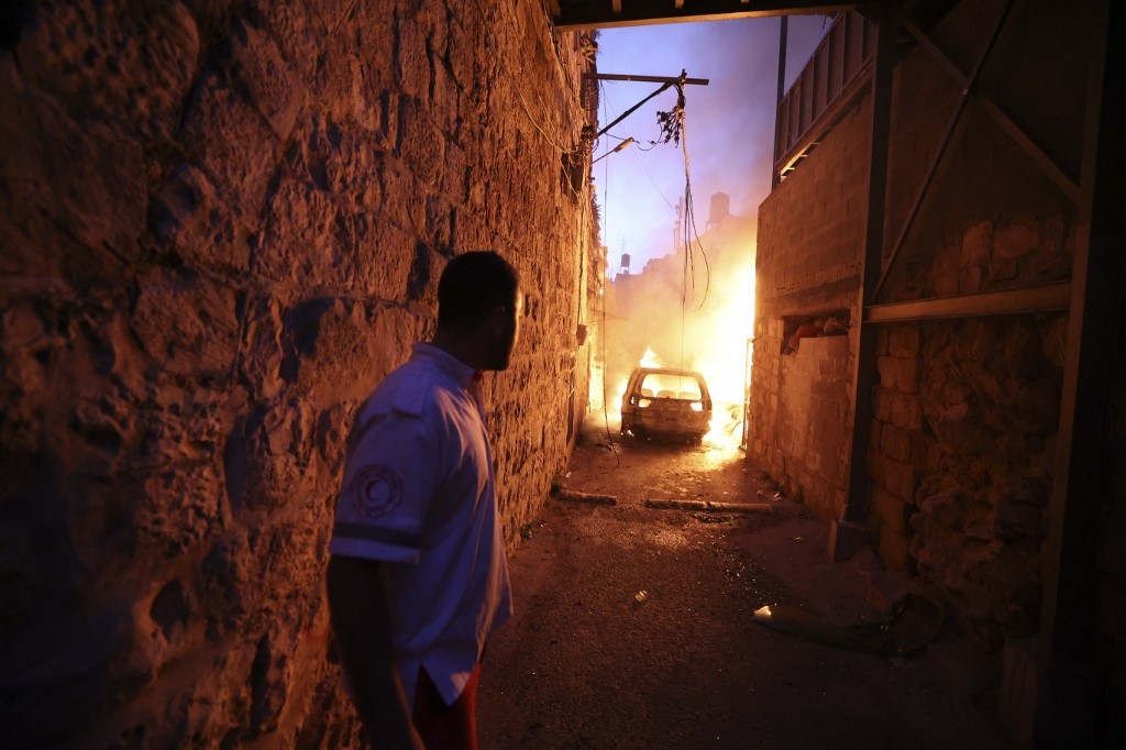 A Palestinian Red Crescent volunteer stands back as fire breaks out in in a house and vehicles during clashes between Israeli troops and Palestinian gunmen in the Old City of Nablus in the northern occupied West Bank early on 24 July 2022. (AFP)