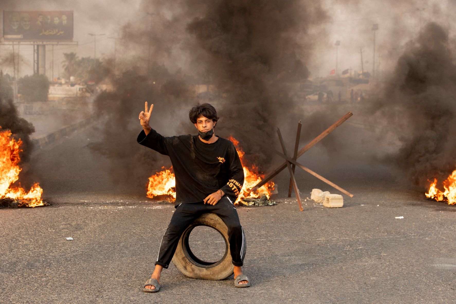 A supporter of Iraqi Shiite cleric Moqtada Sadr poses for a picture on a road blocked with burning tyres during a demonstration in Iraq's southern city of Basra on August 29, 2022 (AFP)
