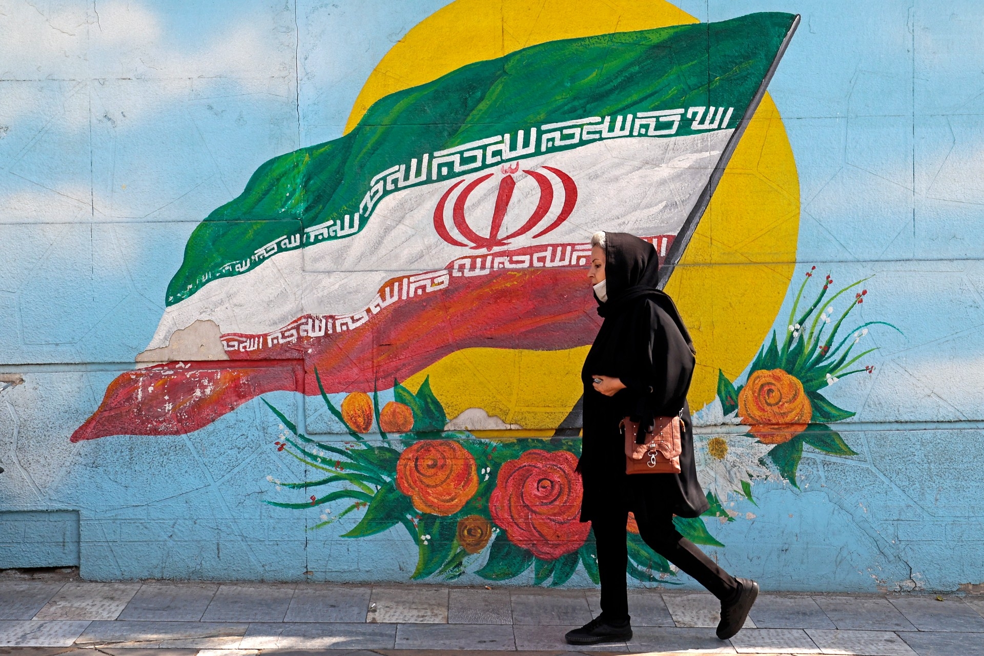 A woman walks past a mural in Tehran, on 11 October (AFP)