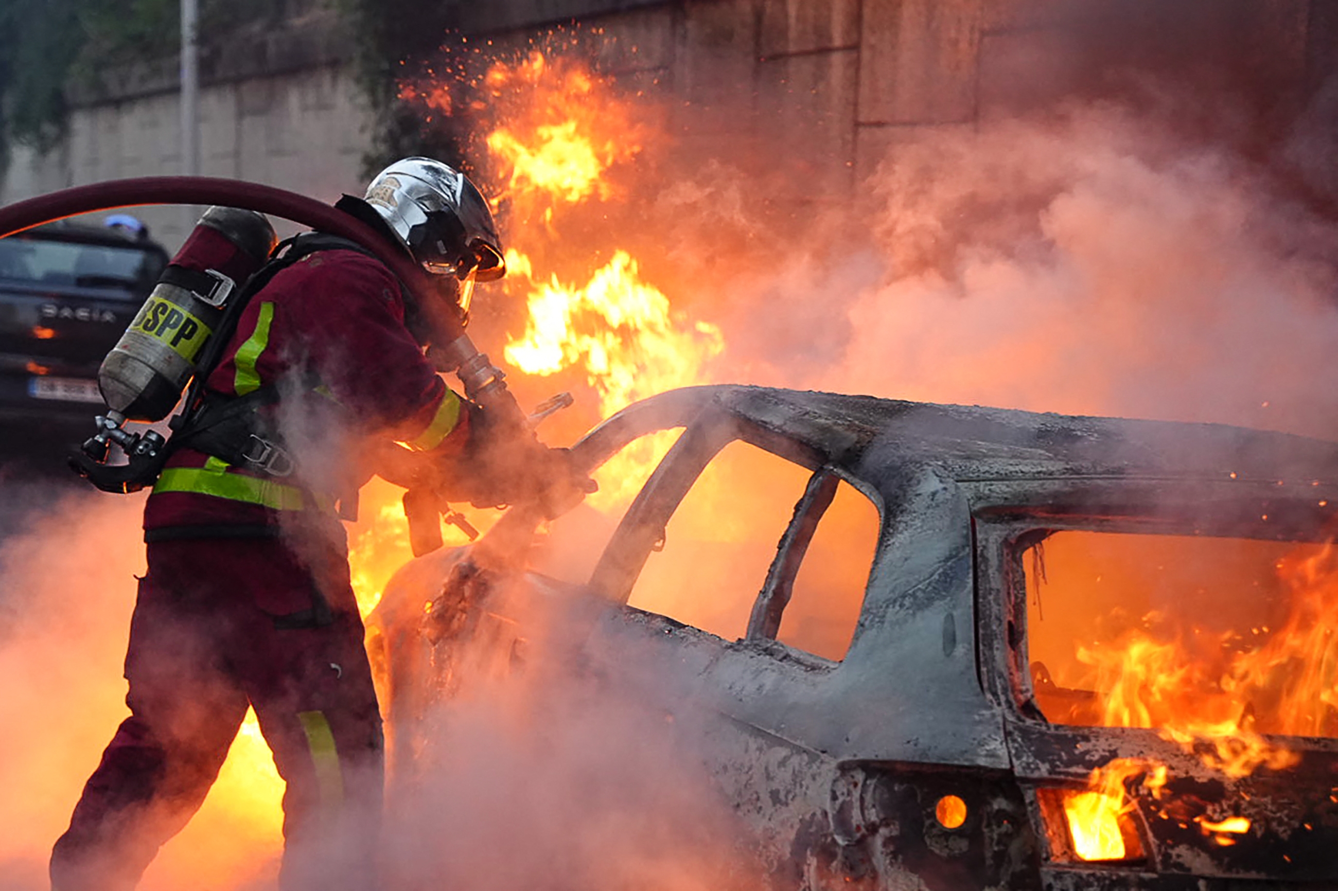 Firefighter extinguish a burning vehicle destroyed during protests in Nanterre, west of Paris, on 27 June (AFP)