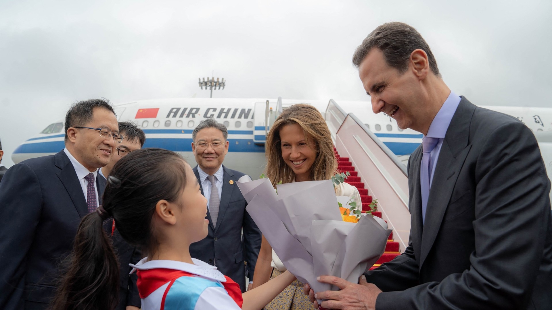 Bashar al-Assad and Asma al-Assad being welcomed upon their arrival at the airport in Beijing, on 21 September (AFP)